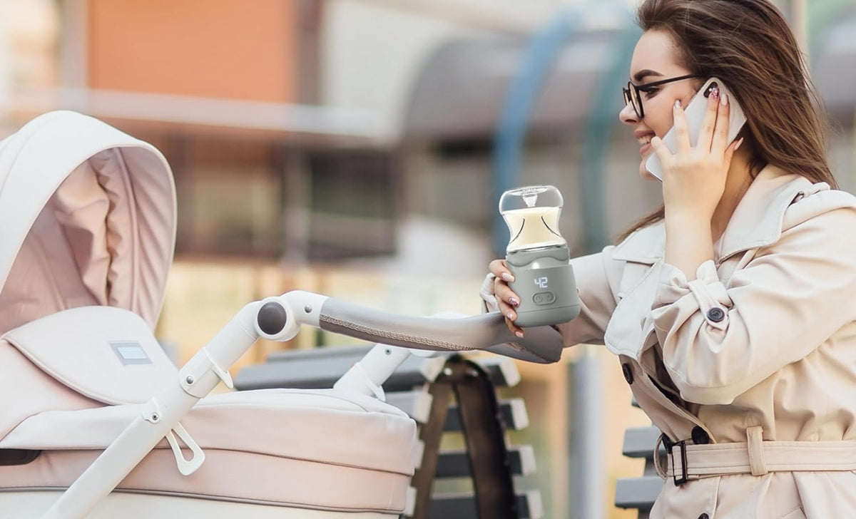 Kobieta stojąca przy wózku trzyma podgrzewacz Nuvita Warm’N’Go z nałożoną butelką i rozmawia przez telefon.