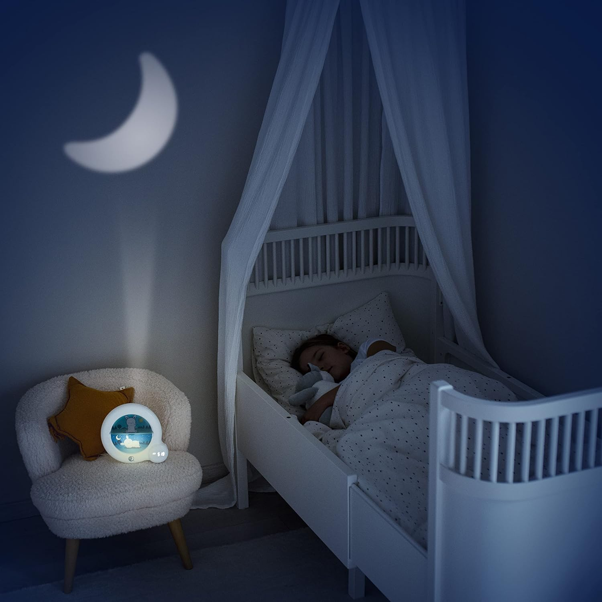 Pabobo Kid'Sleep Essential na krześle przy łóżeczku ze śpiącym dzieckiem, nocna aranżacja pokoju.