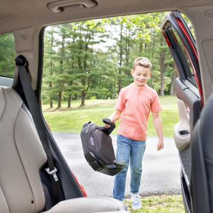 Graco Booster Basic R129 — poglądowe zdjęcie dziecka przenoszącego podstawkę